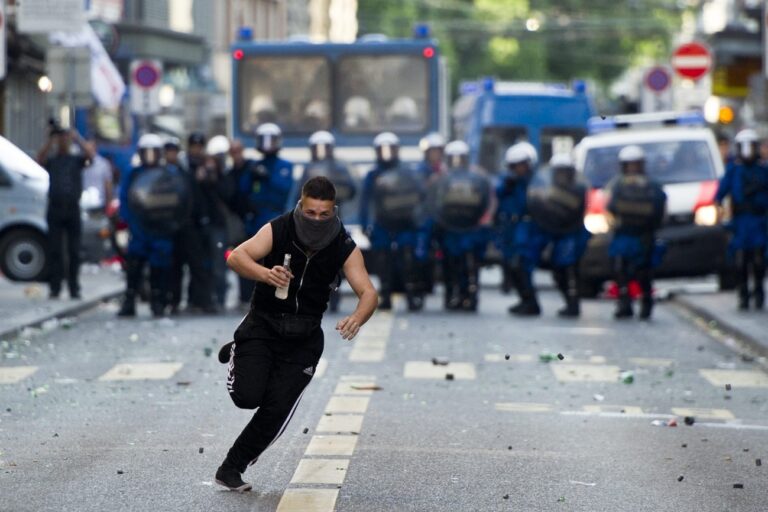 A masked man runs in front of riot police after a labour day demonstration in Zurich, Switzerland, Sunday, on May 1, 2011. (KEYSTONE/Ennio Leanza)