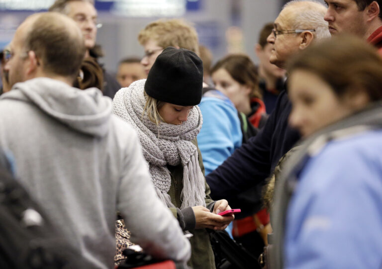 A woman checks her cell phone as she waits at the check-in line in Terminal 3 at O'Hare International Airport in Chicago on Sunday, Jan. 5, 2014. Illinois residents are digging out of more snow and preparing for bitterly cold temperatures. Sunday night temperatures are predicted to drop drastically, to about minus 20 degrees. (AP Photo/Nam Y. Huh)