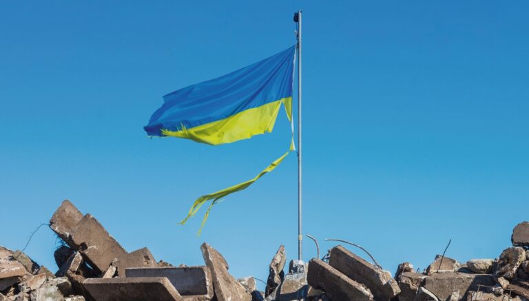 war in ukraine. Destroyed Ukrainian building and damaged flag in the wind.