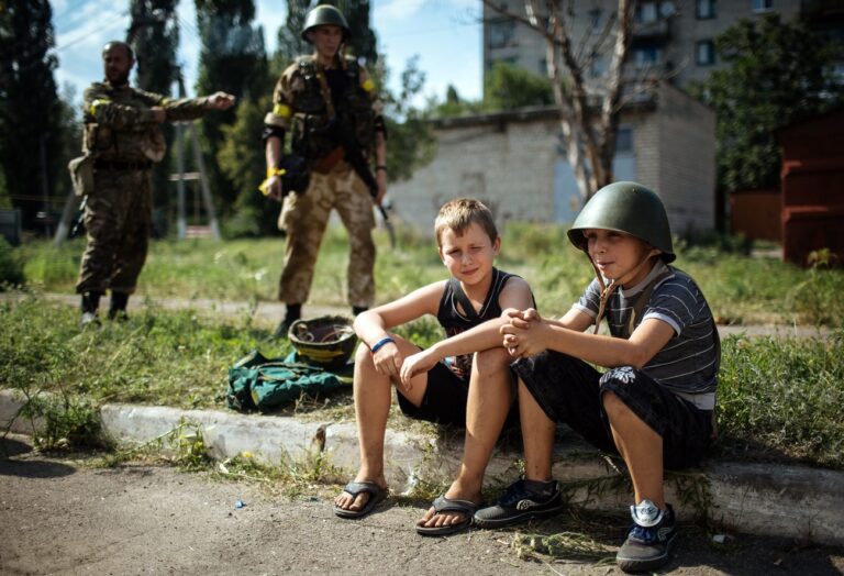 epa04340850 A boy wearing a military helmet sits with his friend near a camp of Ukrainian battalion 'Donbass', which is based in school, during relocation one of the parts from battalion 'Donbass' in the eastern Ukrainian town Popasnaya, in Ukraine, 04 August 2014. A group of international experts managed to reach the Malaysia Airlines plane believed to have been shot down on 17 July by pro-Russian separatists in Ukraine, just as the European Union turned up the heat on Moscow with unprecedented economic sanctions. EPA/ROMAN PILIPEY