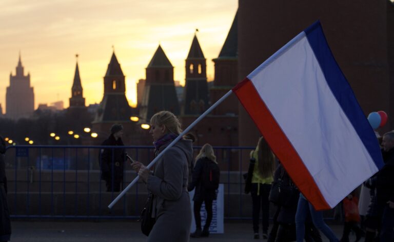 A woman carries a Russian flag after a rally marking the one year anniversary of annexation of Ukraine's Crimea peninsula, outside the Kremlin, in the back, in Moscow, Russia, Wednesday, March 18, 2015. Speaking to tens of thousands of supporters just outside the Kremlin walls, President Vladimir Putin has described Russia's annexation of Ukraine's Crimean Peninsula as a move to protect ethnic Russians and regain the nation's 
