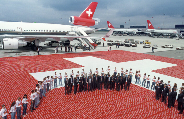 Die Schweizer Fussballnationalmannschaft wird vor ihrem Abflug am 16. Juni 1994 an die Fussball-Weltmeisterschaft in der USA auf dem Flughafen Kloten mit einer riesigen Schweizerfahne verabschiedet. Die Namen von ueber 200'000 Fans stehen auf der Fahne. (KEYSTONE/Str)