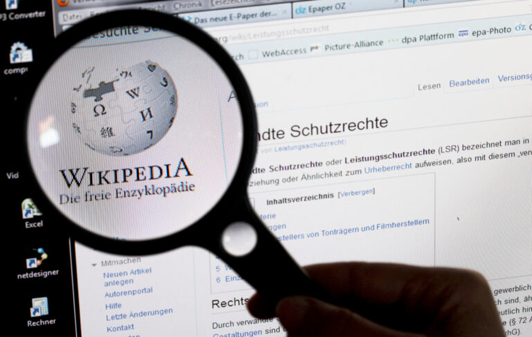 ARCHIV - ILLUSTRATION - Unter einer Lupe ist am 21.06.2012 in Schwerin (Mecklenburg-Vorpommern) der Schriftzug und das Logo des Online-Lexikons Wikipedia auf einem Computerbildschirm zu sehen. (zu dpa: 