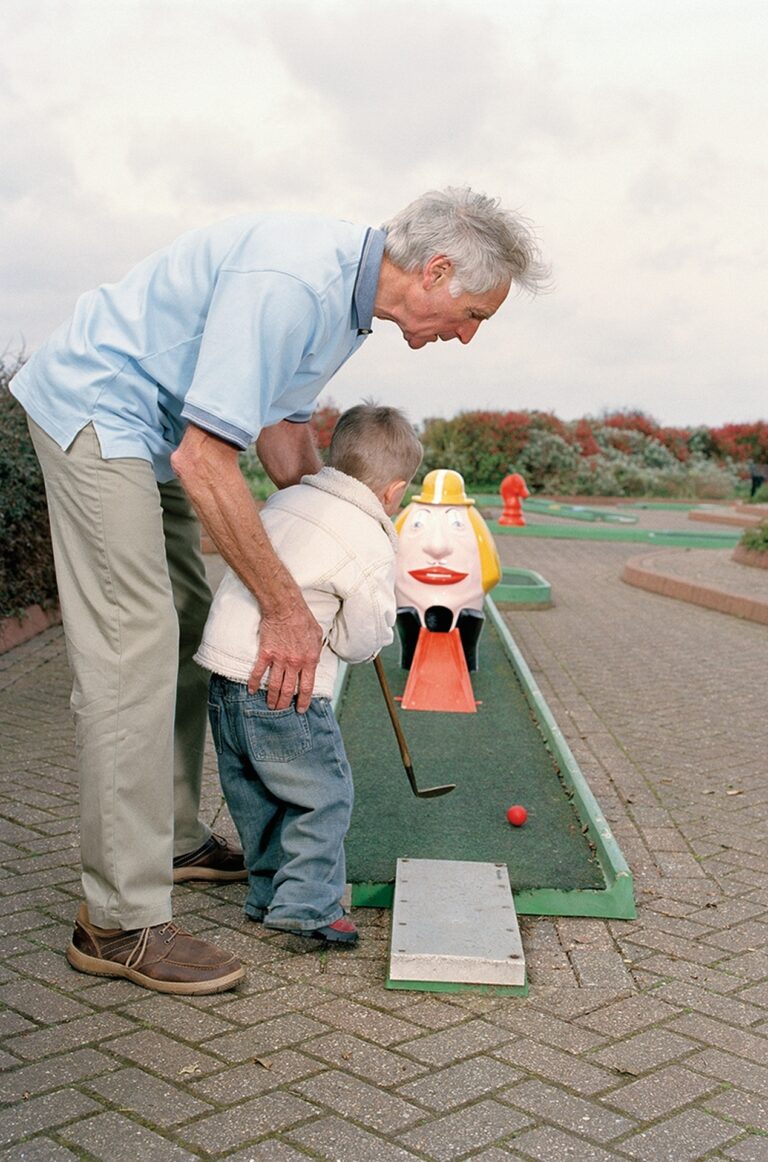 Grandfather helping grandson (3-5) play crazy golf