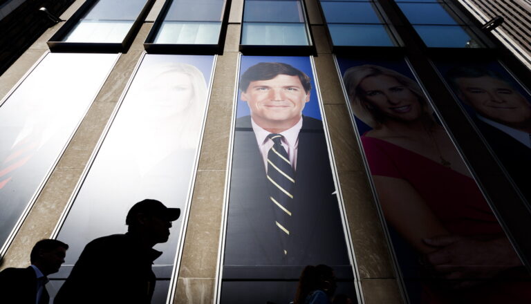 epa07434414 People walk past pictures of Fox News hosts including Tucker Carlson (C) at the studios of Fox News at the News Corporation building in New York, New York, USA, 13 March 2019. Recently compiled recordings of Carlson have lead to widespread allegations that he has regularly used racist and sexist rhetoric. EPA/JUSTIN LANE