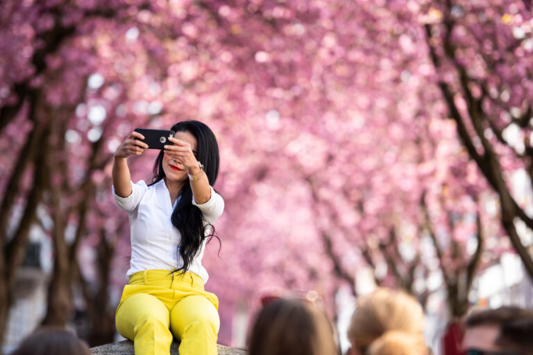 07.04.2019, Nordrhein-Westfalen, Bonn: Eine junge Frau fotografiert sich mit ihrem Handy vor den blühenden Kirschbäume in der Heerstraße. Foto: Marius Becker/dpa +++ dpa-Bildfunk +++ (KEYSTONE/DPA/Marius Becker)