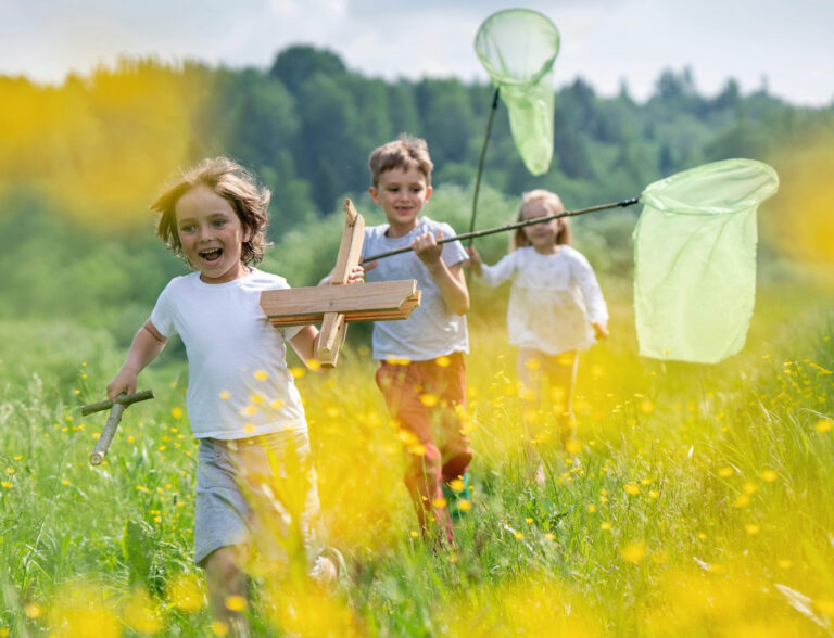 2C8EB9W Carefree friends with model airplane and butterfly nets running on grassy land in forest