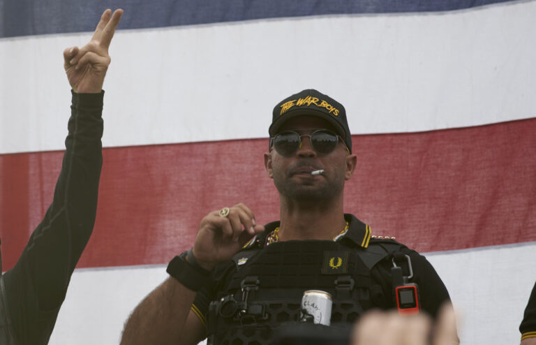 Proud Boys leader Enrique Tarrio wears a hat that says The War Boys and smokes a cigarette at a rally in Delta Park on Saturday, Sept. 26, 2020, in Portland, Ore. (AP Photo/Allison Dinner)