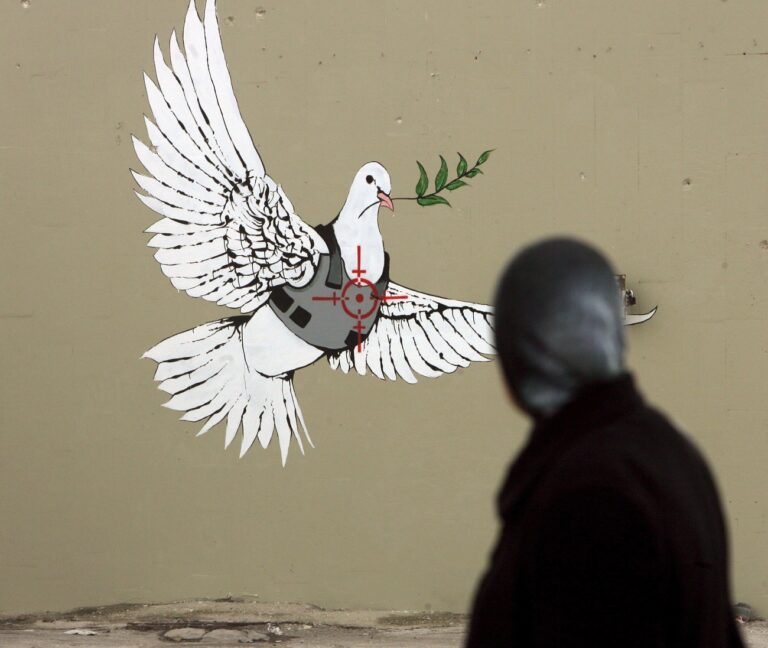 epa01191045 Illusive British graffiti artist named Banksy has painted new works in the West Bank town of Bethlehem, including this Pace dove in a flak jacket as a sniper takes aim at its heart, as a palestinian woman passes and looks at the work on a Bethlehem street corner on 04 December 2007. Banksy does not sign his works and no one knows the identity of the guerrila artist, but he works have been known to fetch huge sums in gallery sales. These new works are being dubbed 'West Banksy,' and some are painted on the controversial Israeli 'separation barrier,' or wall, that surrounds Bethlehem and cuts its residents off from nearby Jerusalem. EPA/JIM HOLLANDER