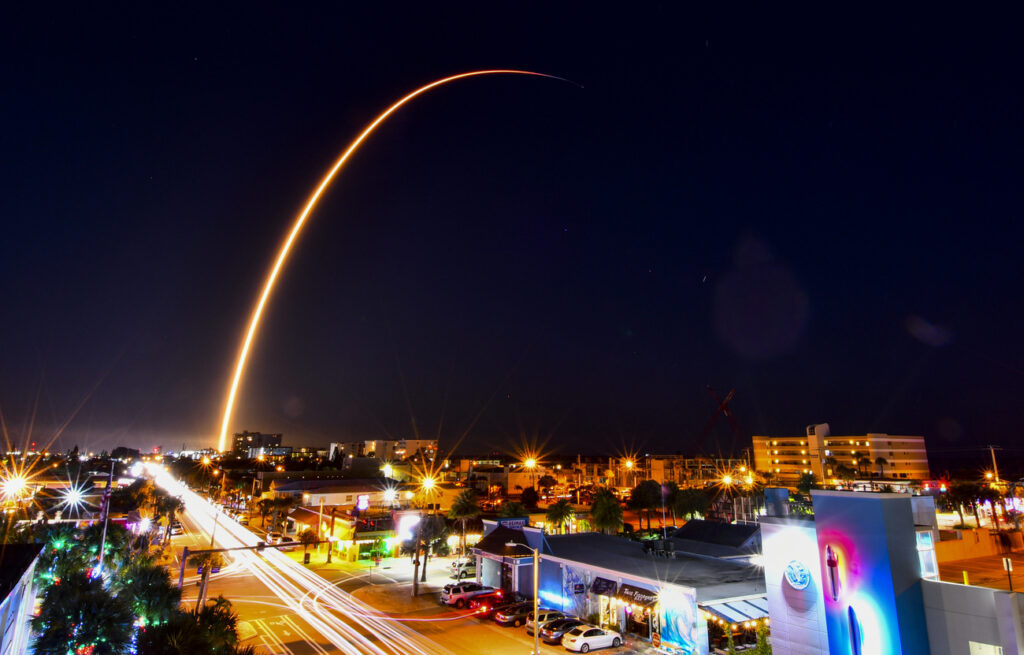 In this image taken with a long exposure, a SpaceX Falcon 9 rocket carrying the 32nd batch of Starlink internet satellites arches over the skyline of Cocoa Beach, Fla., Thursday evening, Dec. 2, 2021, after blasting off from Cape Canaveral. (Malcolm Denemark/Florida Today via AP)