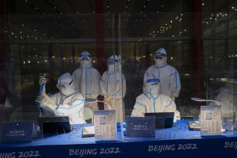 Olympic workers in hazmat suits work at a credential validation desk at the Beijing Capital International Airport ahead of the 2022 Winter Olympics in Beijing, Monday, Jan. 24, 2022. (KEYSTONE/AP Photo/Jae C. Hong)