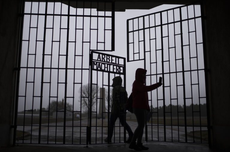 Persons take photos as they enter the Sachsenhausen Nazi death camp through the gate with the phrase 'Arbeit macht frei' (work sets you free), in Oranienburg, about 30 kilometers (18 miles) north of Berlin, Germany, Tuesday, Jan. 25, 2022. On Thursday Jan. 27, 2022 the International Holocaust Remembrance Day marks the liberation of the Auschwitz Nazi death camp on Jan. 27, 1945. (AP Photo/Markus Schreiber)