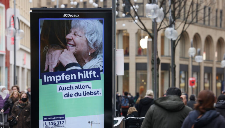 10.02.2022, Nordrhein-Westfalen, Köln: Menschen gehen an einerelektronischen Werbetafel mit der Aufschrift 