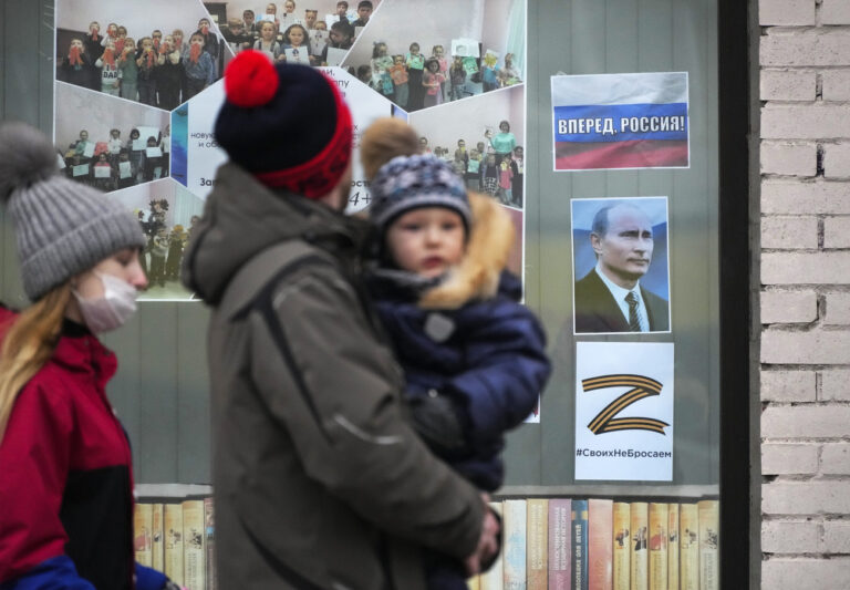 FILE - A family walk past a portrait of Russian President Vladimir Putin, a sign reading 'Go Russia!' and the letter Z, which has become a symbol of the Russian military, displayed in the window of a children's library in St. Petersburg, Russia, Friday, March 11, 2022. (AP Photo, File)