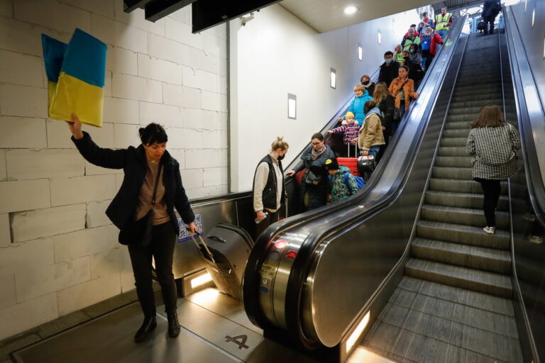 epa09842578 A volunteer holds a Ukrainian flag to guide refugees fleeing Ukraine following the Russian invasion from a platform as they arrive by train from Germany to Belgium at Midi Station in Brussels, Belgium, 22 March 2022. Brussels' Midi station very often is the the point of arrival for the Ukrainian refugees. After their arrival they are sent to the refugee center to be registered in order to have protection for at least one year. EPA/STEPHANIE LECOCQ