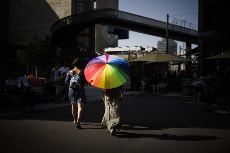 A woman walks in the streets with a rainbow colored umbrella after the Zurich Pride parade with the slogan 