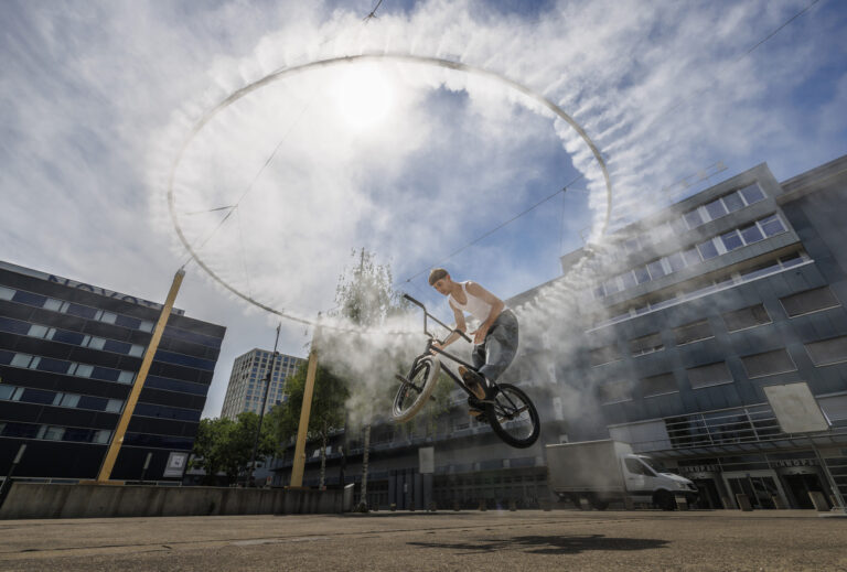 Basil Roos zeigt mit seinem BMX einen Trick unter der neuerrichteten Nebelwolke auf dem Turbinenplatz, aufgenommen am Donnerstag, 30. Juni 2022 in Zuerich. Die kuenstlich erzeugte Nebelwolke soll an heissen Tagen fuer Abkuehlung sorgen. (KEYSTONE/Michael Buholzer)