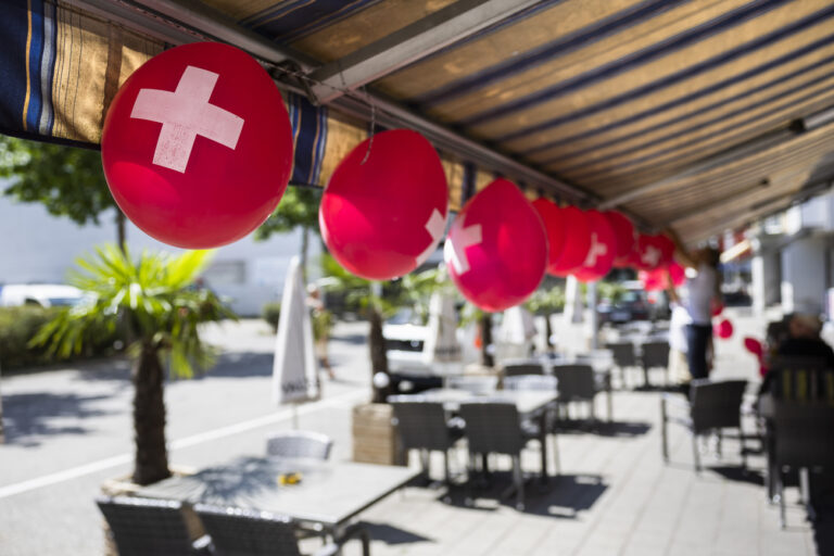 Mitarbeiterinnen eines Restaurants verzieren die Terrasse mit Luftballonen mit einem Schweizer Kreuz, am Montag, 1. August 2022 in Grenchen. (KEYSTONE/Peter Klaunzer)