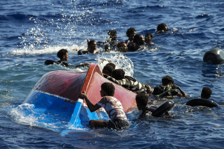 Migrants swim next to their overturned wooden boat during a rescue operation by Spanish NGO Open Arms at south of the Italian Lampedusa island at the Mediterranean sea, Thursday, Aug. 11, 2022. Forty migrants from Eritrea and Sudan, two children and one woman, were rescued by NGO Open Arms crew members and Italian coast guard after their boat overturned and started to sink. (AP Photo/Francisco Seco)