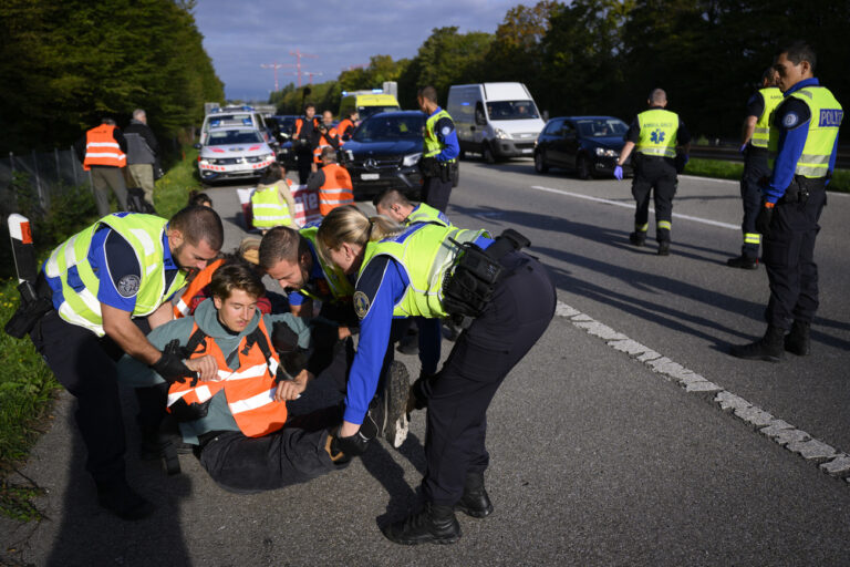 Police officers arrest environmental activist member of Renovate Switzerland after he sit down in the road during a roadblock action of the A1a motorway, in Lausanne, Switzerland, Tuesday, October 4, 2022.(KEYSTONE/Laurent Gillieron)