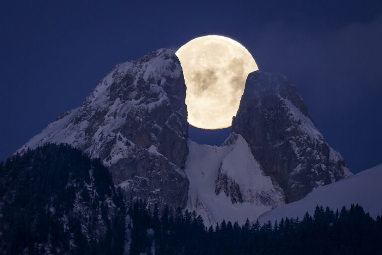 The full moon sets behind the mountains including the twin peaks of Les Jumelles in the Chablais Valaisan, on Monday, 6 February 2023, seen from Aigle, Switzerland. (KEYSTONE/Anthony Anex)