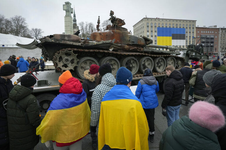 People watch a destroyed Russian tank T-72B, installed as a symbol of the Russia Ukraine war to mark the first anniversary of Russia's full-scale invasion of Ukraine in Tallinn, Estonia, Saturday, Feb. 25, 2023. (AP Photo/Sergei Grits)