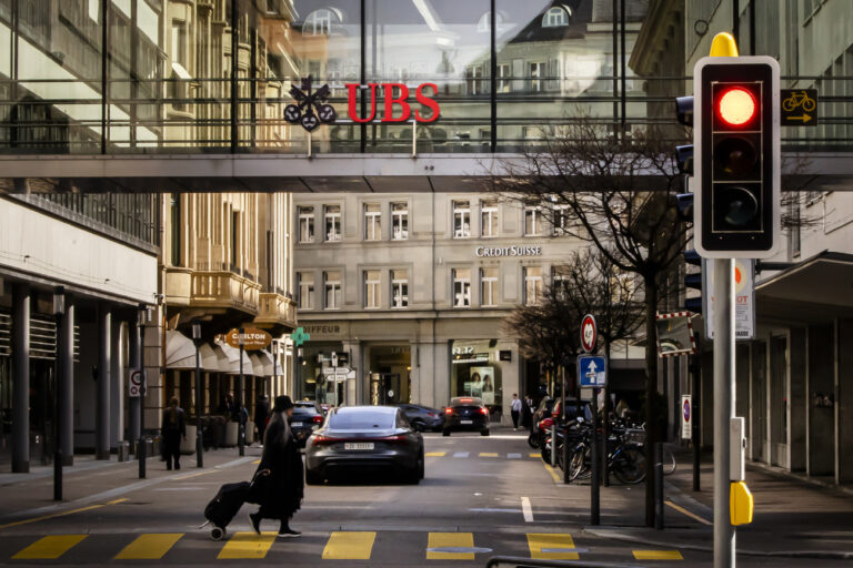 A woman crosses a road as logos of the Swiss banks Credit Suisse and UBS are displayed on buildings in Zurich, Switzerland on Saturday, March 18, 2023. (KEYSTONE/Michael Buholzer).