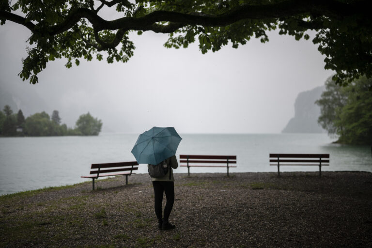 Eine Frau mit Schirm steht bei starkem Regen am Walensee, am Dienstag, 16. Mai 2023, in Weesen. (KEYSTONE/Gian Ehrenzeller)