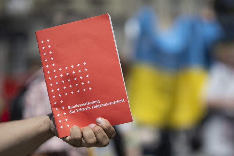 A participant holds the Swiss constitution in his hand front of a Ukrainian flag just after the broadcast of the Ukrainian President Volodymyr Zelensky's speech to the members of the Swiss parliament, front of the Federal Palace, in Bern, Switzerland, Thursday, June 15, 2023. (KEYSTONE/Anthony Anex)
