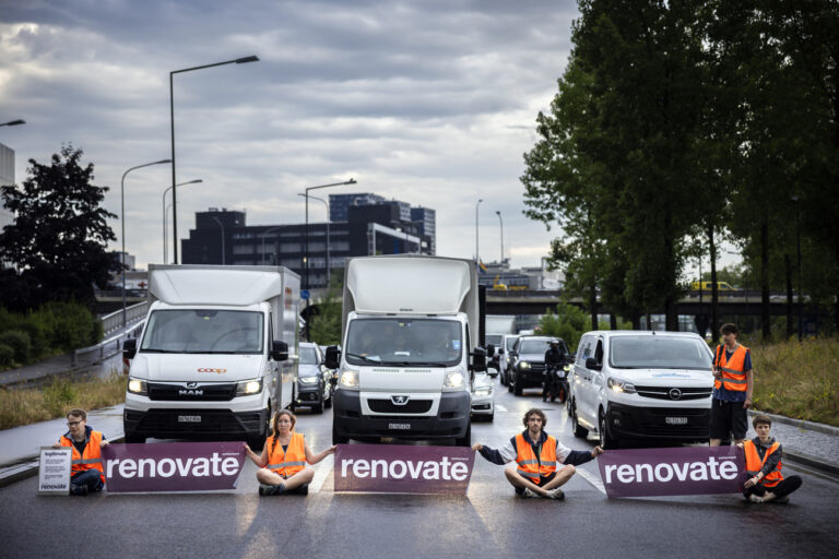 Environmental activists of Renovate Switzerland sit down on the road during a roadblock action on the motorway A1 exit in Zuerich, Switzerland on June 19, 2023. (KEYSTONE/Michael Buholzer).