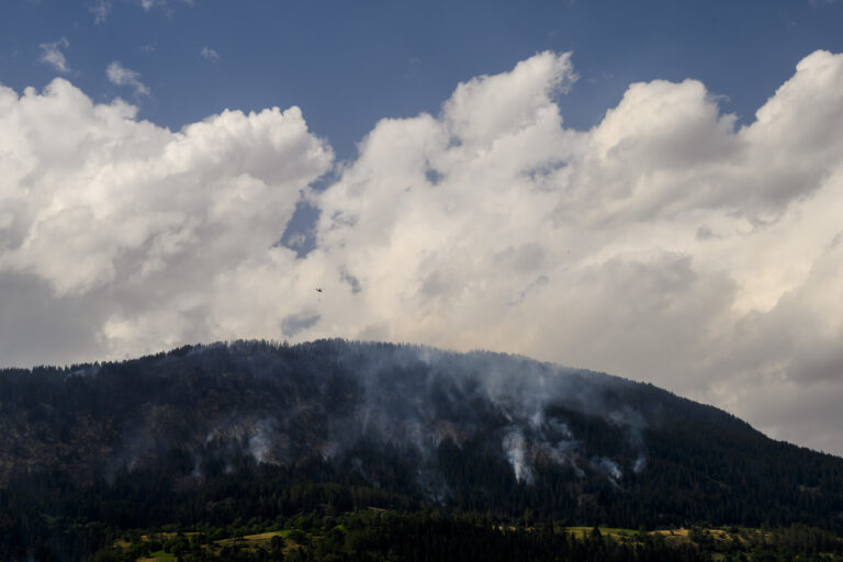 Un helicoptere Super Puma verse de l'eau sur la fumee qui s'echappe de la foret en feu au dessus des communes de Bitsch et Ried-Moerel le mardi 18 juillet 2023 depuis Termen. Les hélicopteres ont vole durant toute la nuit de lundi a mardi pour lutter contre l'incendie de foret qui fait rage dans le Haut-Valais. Les operations d'extinction devraient durer plusieurs jours. (KEYSTONE/Jean-Christophe Bott)