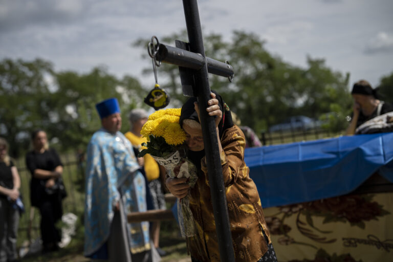 Nadiia, grandmother of Ukrainian soldier Oleksander Mykhailenko, holds the cross at the grave where her grandson will be buried in Zhukin, Ukraine, Friday, Aug. 11, 2023. Oleksander, a soldier in the Ukrainian army, died in battle in the Kharkiv region in March this year but his body was only identified recently. (AP Photo/Bram Janssen)