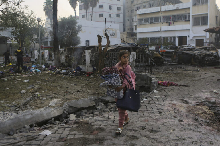 A girl carries blankets as she walks past the site of a deadly explosion at al-Ahli Hospital in Gaza City, Wednesday, Oct. 18, 2023. (AP Photo/Abed Khaled)