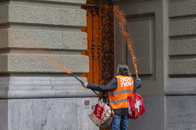 Ein Klimaaktivist von Renovate Switzerland besprueht die Eingangstueren des Bundeshauses mit oranger Farbe, am Donnerstag, 8. Februar 2024, in Bern. (KEYSTONE/Peter Schneider)