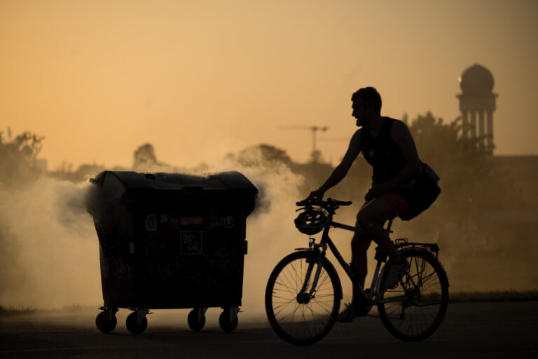 15.05.2024, Berlin: Ein Fahrradfahrer fährt vor Sonnenuntergang auf dem Temepelhofer Feld an einem qualmenden Mülleimer nahe des Grillplatzes vorbei. Der Brand wurde kurz darauf von Sicherheitsleuten gelöscht. Foto: Sebastian Gollnow/dpa +++ dpa-Bildfunk +++ (KEYSTONE/DPA/Sebastian Gollnow)