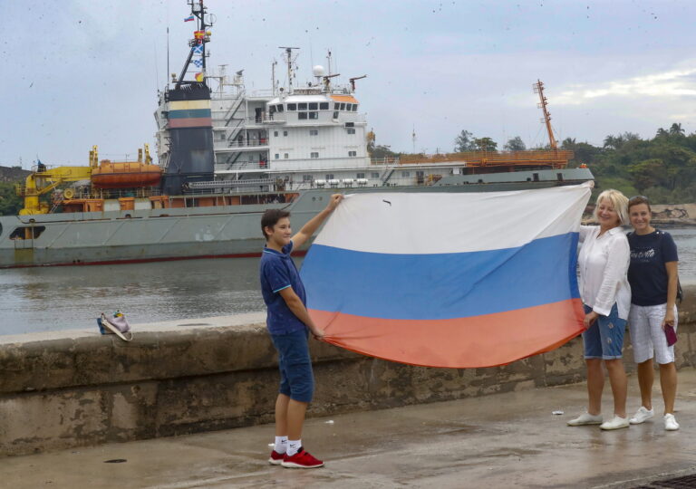 epa11406313 Russian nationals hold a flag during the arrival of a ship belonging to the Russian Navy flotilla at the port of Havana, in Havana, Cuba, 12 June 2024. A Russian Navy flotilla including a modern frigate and a nuclear-powered submarine arrived in Havana as part of a scheduled visit. EPA/Yander Zamora