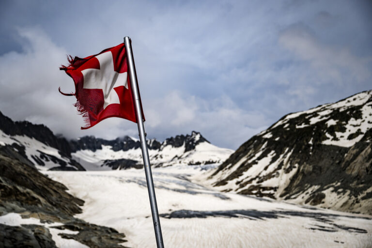 Un drapeau Suisse est visible devant le glacier du Rhone le mercredi 26 juin 2024 entre Gletsch et le Col de la Furka en Valais. Avec la fonte du glacier du Rhone, suite aux changements climatiques, le lac glaciaire du Rhone devient plus grand. (KEYSTONE/Jean-Christophe Bott)