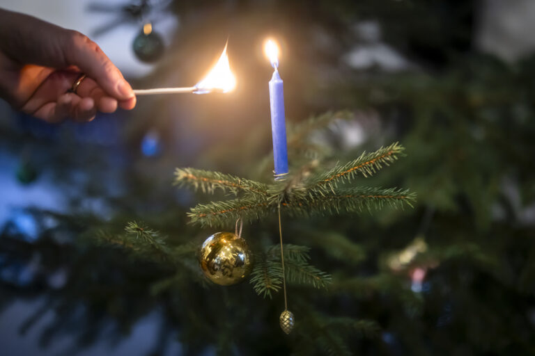 Eine Person zuendet eine Kerze an einem Weihnachtsbaum an, aufgenommen am Samstag, 14. Dezember 2024 in Zuerich. (KEYSTONE/Michael Buholzer).