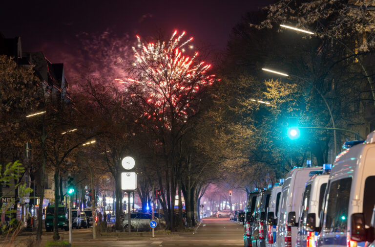 31.12.2024, Berlin: Fahrzeuge der Polizei stehen in der Sonnenallee im Stadtbezirk Neukölln in der Verbotszone für Feuerwerk. Im Hintergrund außerhalb der Zone ist am Himmel Feuerwerk zu sehen. Foto: Soeren Stache/dpa +++ dpa-Bildfunk +++ (KEYSTONE/DPA/Soeren Stache)