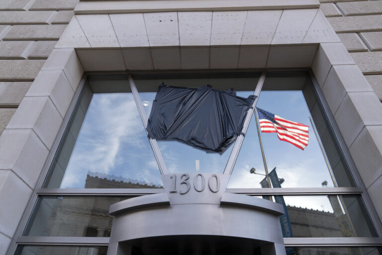 The American flag flying alone beside an empty flagpole that previously had the flag of the U.S. Agency for International Development, or USAID, are pictured in the reflection of a window that previously had the sign and the seal of USAID, outside the agency's headquarters in Washington, Friday, Feb. 7, 2025. (AP Photo/Jose Luis Magana)