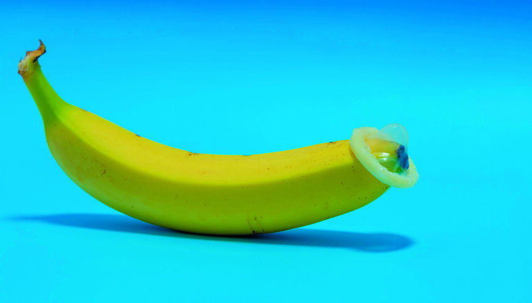 2M1RYJ1 A banana with a condom on a blue background